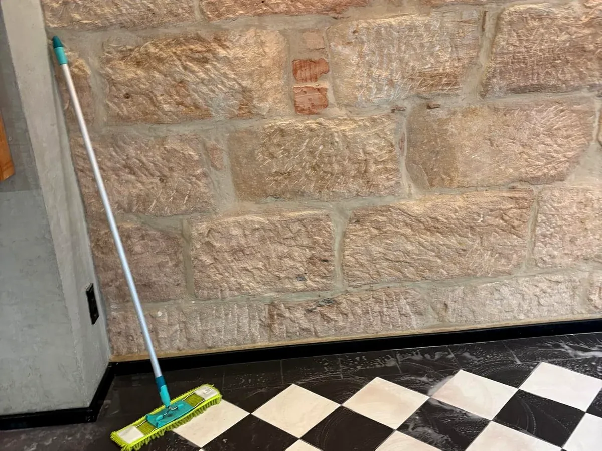 Reinigung einer Bodenfläche entlang einer Natursteinwand.