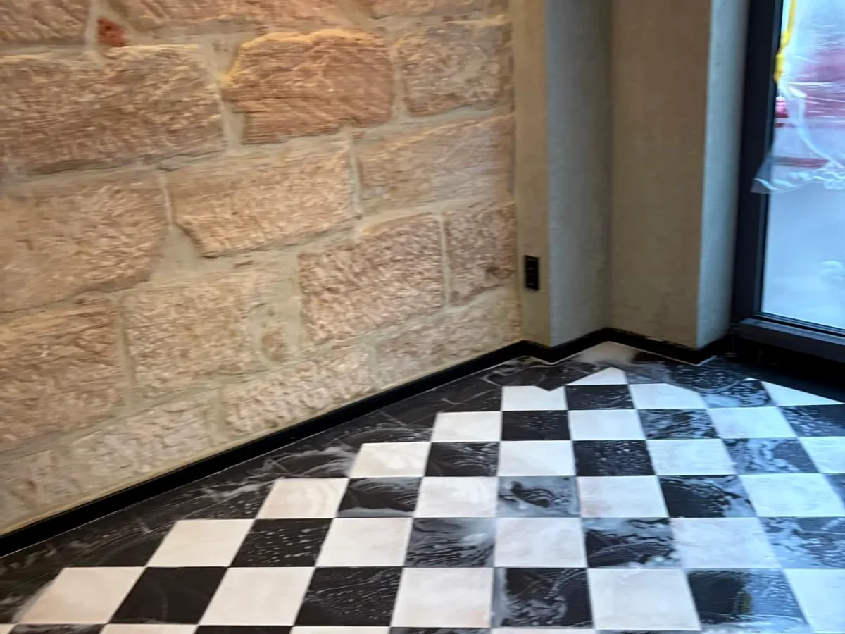 Nass gereinigte Bodenfläche in einem Innenbereich mit Natursteinwand.